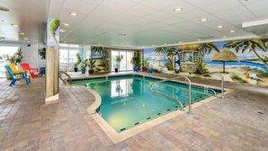 An indoor swimming pool with a tropical mural, colorful lounge chairs, and potted plants.