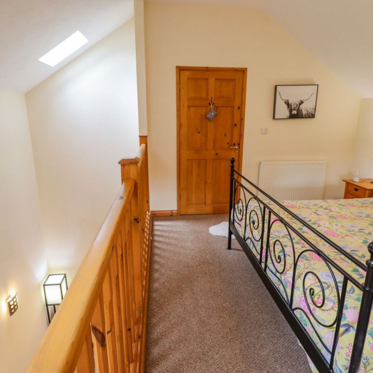 A bedroom with a wooden door, a bed with a floral bedspread, a radiator, and a small bedside table.