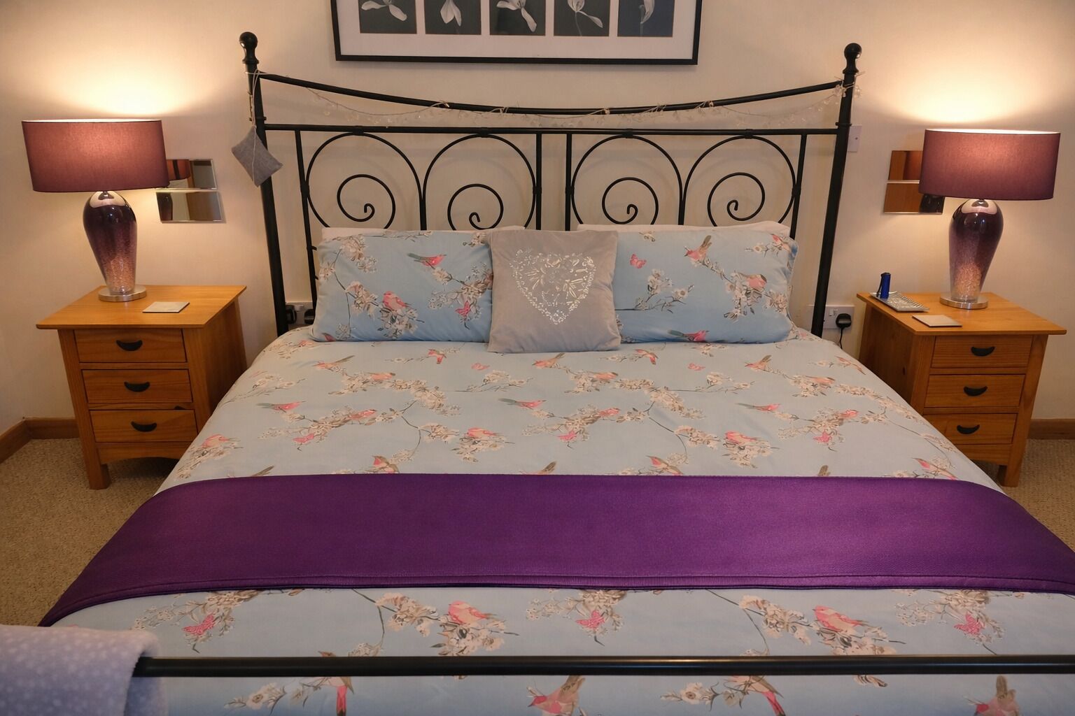 A bed with floral bedding, two bedside tables with lamps, and a headboard.