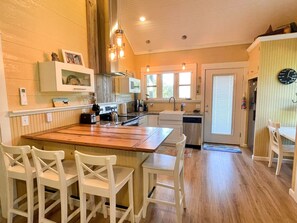 A kitchen with a wooden island, white chairs, a sink, and a refrigerator.