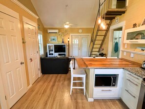 A compact kitchen with a wooden countertop, white cabinetry, and a built-in microwave.