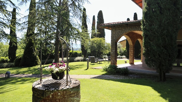 Un jardín con una fuente de piedra, un pérgola y un edificio con entrada arqueada.