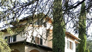 Una casa de dos pisos con fachada de piedra, un árbol grande en el frente y un césped bien cuidado.