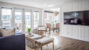 Un salon lumineux avec un canapé, des fauteuils, une table à manger et un téléviseur fixé au mur.