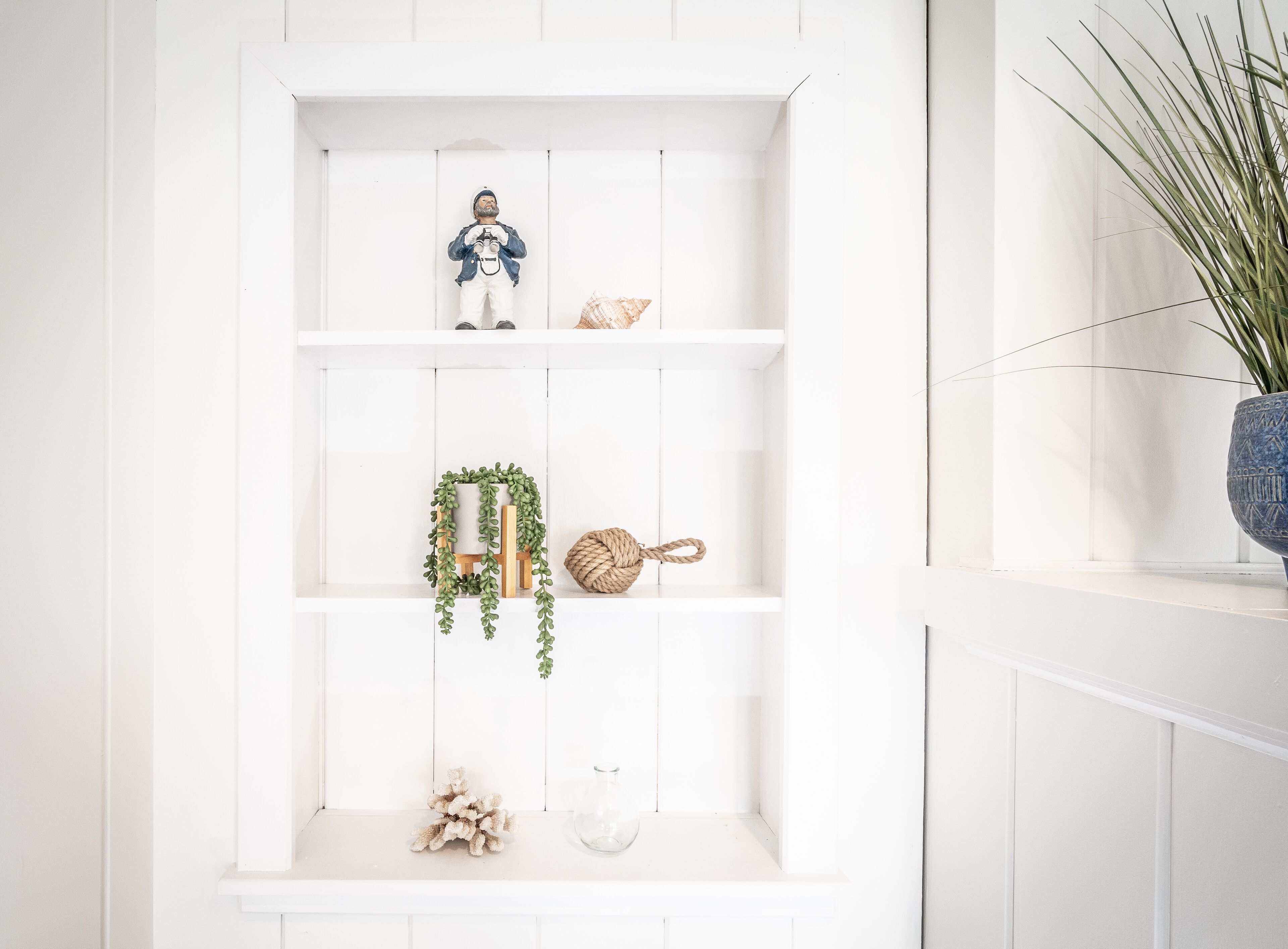A white wooden shelf with various decorative items including a figurine, a woven basket, and a plant.