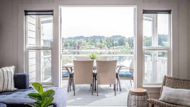 Une pièce avec vue sur un lac et des collines, comprenant un canapé, une table à manger avec des chaises et un petit tabouret.