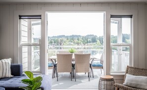 A room with a view of a lake and hills, featuring a sofa, a dining table with chairs, and a small stool. - Gorgeous Waterfront home sleeps 6! Outdoor fireplace, HOT TUB & a large yard! (Bremerton)