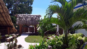 Une construction à toit de chaume, un chemin pavé et une végétation tropicale luxuriante.