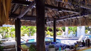 Un espace aménagé au bord de la piscine, doté d’un toit de chaume, de chaises longues et d’une piscine.