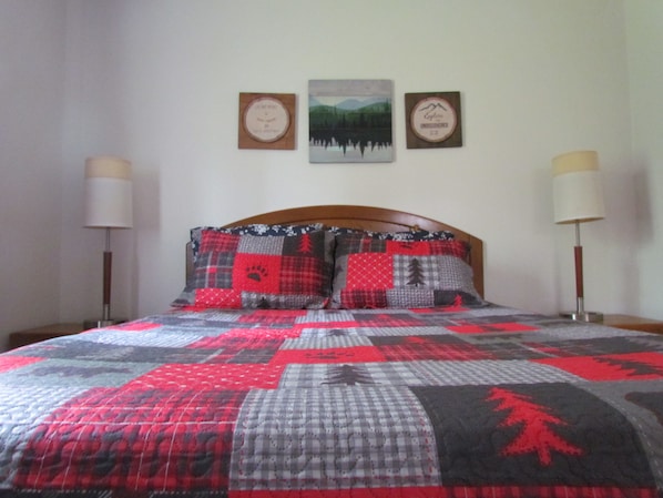 A bed with a quilted bedspread featuring a patchwork design, flanked by two bedside lamps and three framed pictures on the wall above.