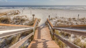 Ein Holzsteg führt zu einem Sandstrand mit freiem Blick auf das Meer.