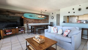 Ein Wohnzimmer mit Fernseher, Couchtisch aus Holz und einem hellblauen Sofa mit gemusterten Kissen.