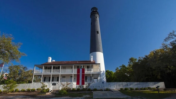 A lighthouse with a white and black tower, a two-story building with a balcony, and a white picket fence.