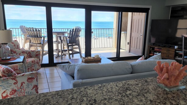 Ein Wohnzimmer mit Sofa, Sesseln, Fernseher und Meerblick durch große Glaswände.