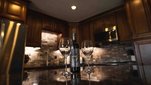 Une cuisine avec des meubles de rangement en bois, un réfrigérateur en acier inoxydable et une bouteille de vin accompagnée de deux verres.