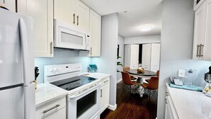 A compact kitchen with white cabinetry, a built-in microwave, a stove, and a dining area with a table and chairs. - Near UF and SHANDS Hospital cozy spot (Gainesville)