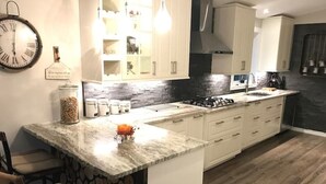 Una cucina moderna con un piano di lavoro in marmo, mobili bianchi e una parete decorata con pietra.