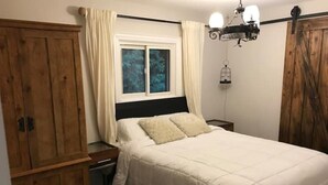 Camera da letto con un letto, un armadio in legno, una finestra con tende, un comodino e una lampada a sospensione.