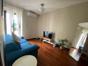 A living room with a blue sofa, a TV on a stand, a small table, a mirror, and a potted plant. - Lovely appartment at the heart of La Spezia (La Spezia)
