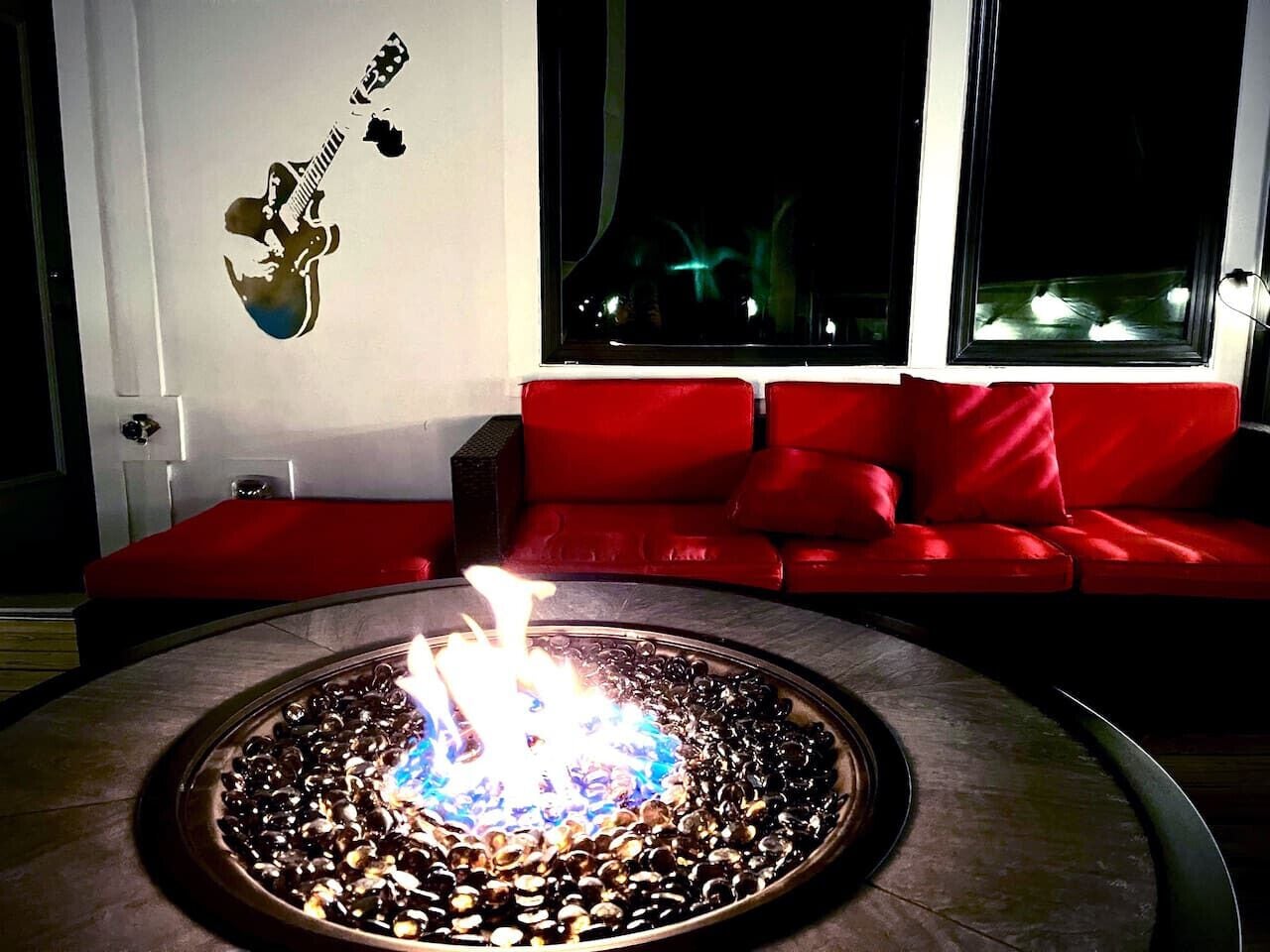A living room with a circular fire feature, a red sofa, and a wall-mounted guitar decoration.