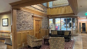 A lobby with a stone wall, wooden paneling, a bench, two patterned armchairs, and a glass door leading outside. - King Bed Condo at Cedar Breaks Lodge (Brian Head)