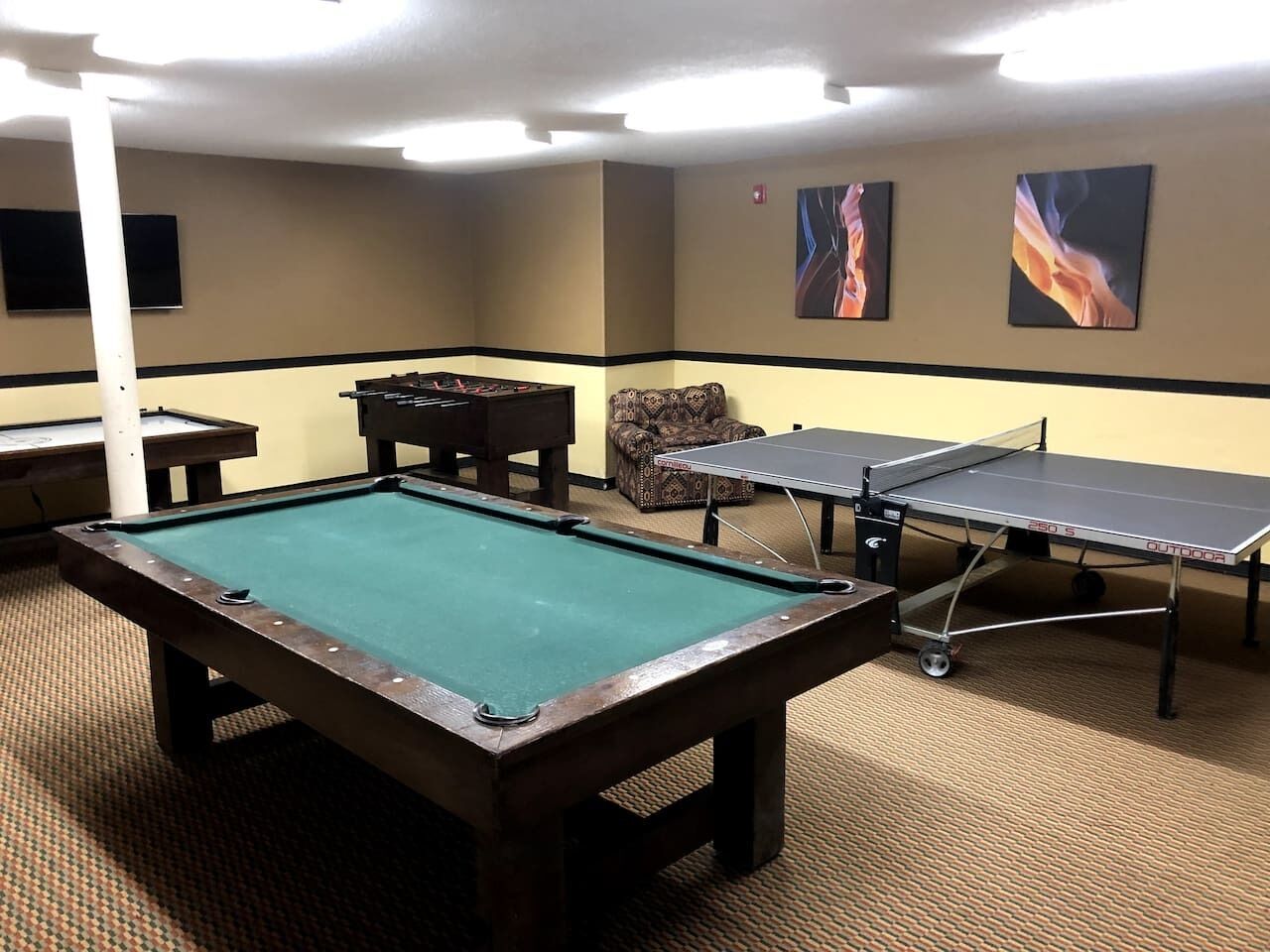 A pool table, two ping pong tables, a sofa, and artwork on the walls.