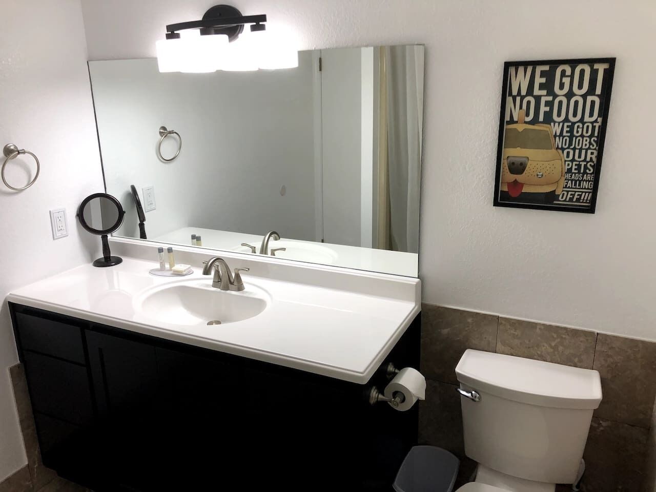 A bathroom with a white sink, a large mirror, a toilet, and a poster on the wall.