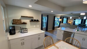A modern kitchen with white cabinets, a coffee maker, a toaster, and a dining table with chairs. - Vacation Rental on Siesta Key (Siesta Key)