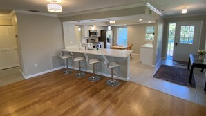 A modern kitchen with a central island, bar stools, and a dining area with a table and chairs. - Vacation Rental on Siesta Key (Siesta Key)