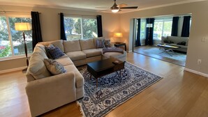 A spacious living room with a large sectional sofa, a coffee table, and a patterned rug. There is a ceiling fan and a view of the outdoors through large windows. - Vacation Rental on Siesta Key (Siesta Key)