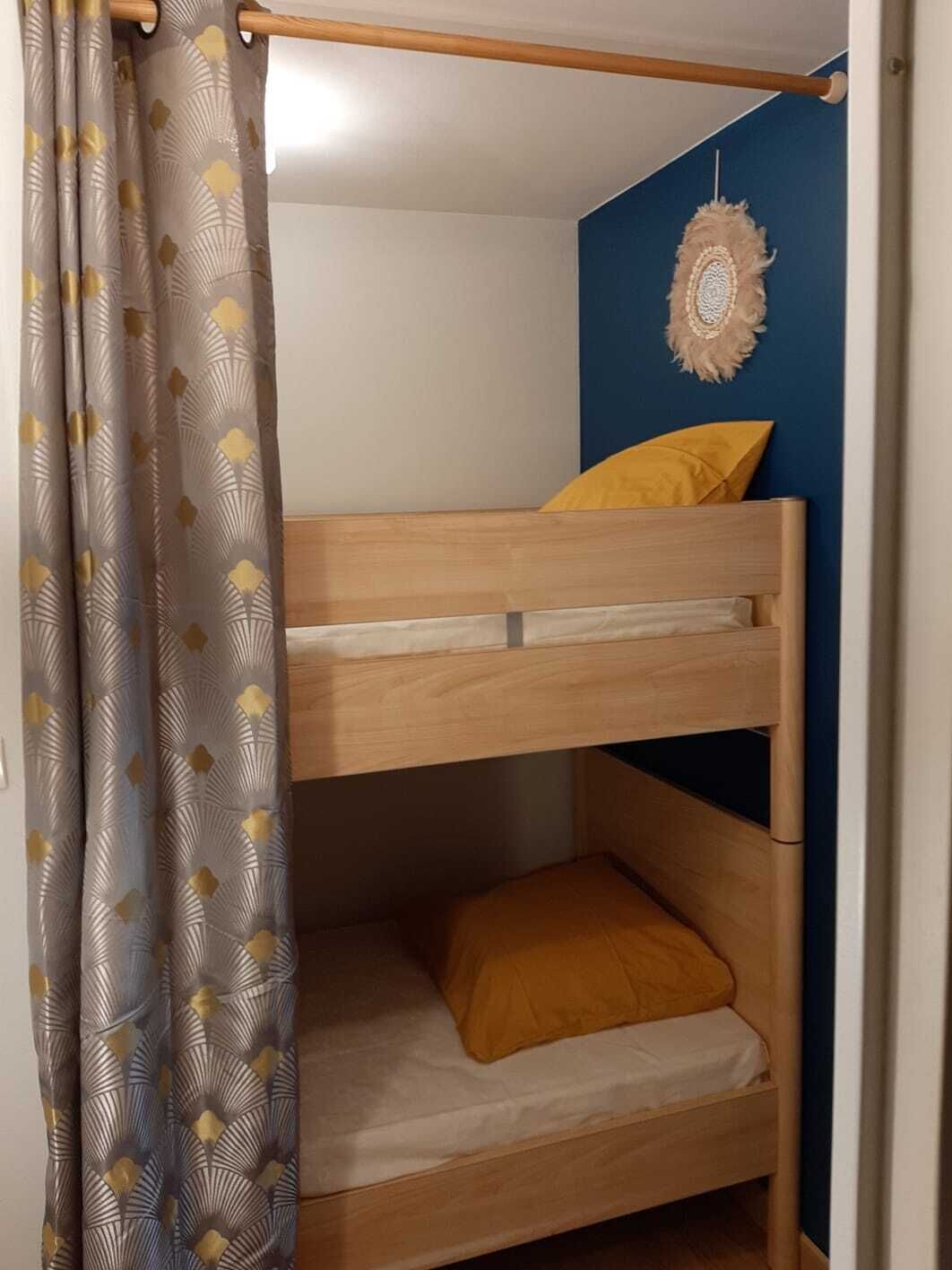 Un lit superposé avec une structure en bois, un oreiller jaune et un rideau à motifs.
