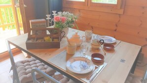 A wooden cabin interior with a dining table set for four, featuring a vase of flowers, tea set, and a box of chocolates. - Wooden chalet with magnificent view (Neuviller-la-roche)