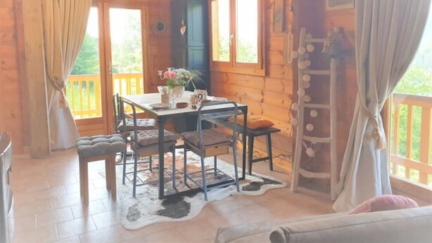 A cozy cabin interior with a dining table set for four, a blue cabinet, and a view of the outdoors through large windows. - Wooden chalet with magnificent view (Neuviller-la-roche)