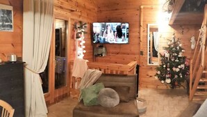 A cozy log cabin interior with a wooden floor, a brown sofa, a television, a Christmas tree, and a dining area with a table and chairs. - Wooden chalet with magnificent view (Neuviller-la-roche)