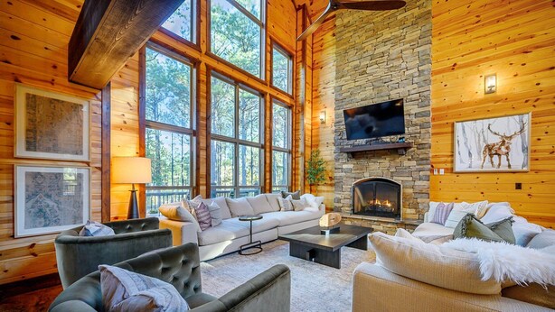 L’intérieur chaleureux d’un chalet en bois avec une cheminée en pierre, de grandes fenêtres et un coin salon confortable.