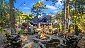 Une cabane avec un foyer entouré de fauteuils Adirondack, située dans une zone boisée.