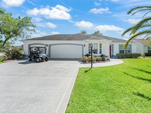 A residential house with a garage, a golf cart, and a well-maintained lawn.