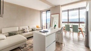 A modern living room with a sofa, a dining area with chairs, and a large window offering a view.