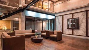 A modern lobby with a staircase, a large 'NEST' sign, and a seating area with sofas and a coffee table.