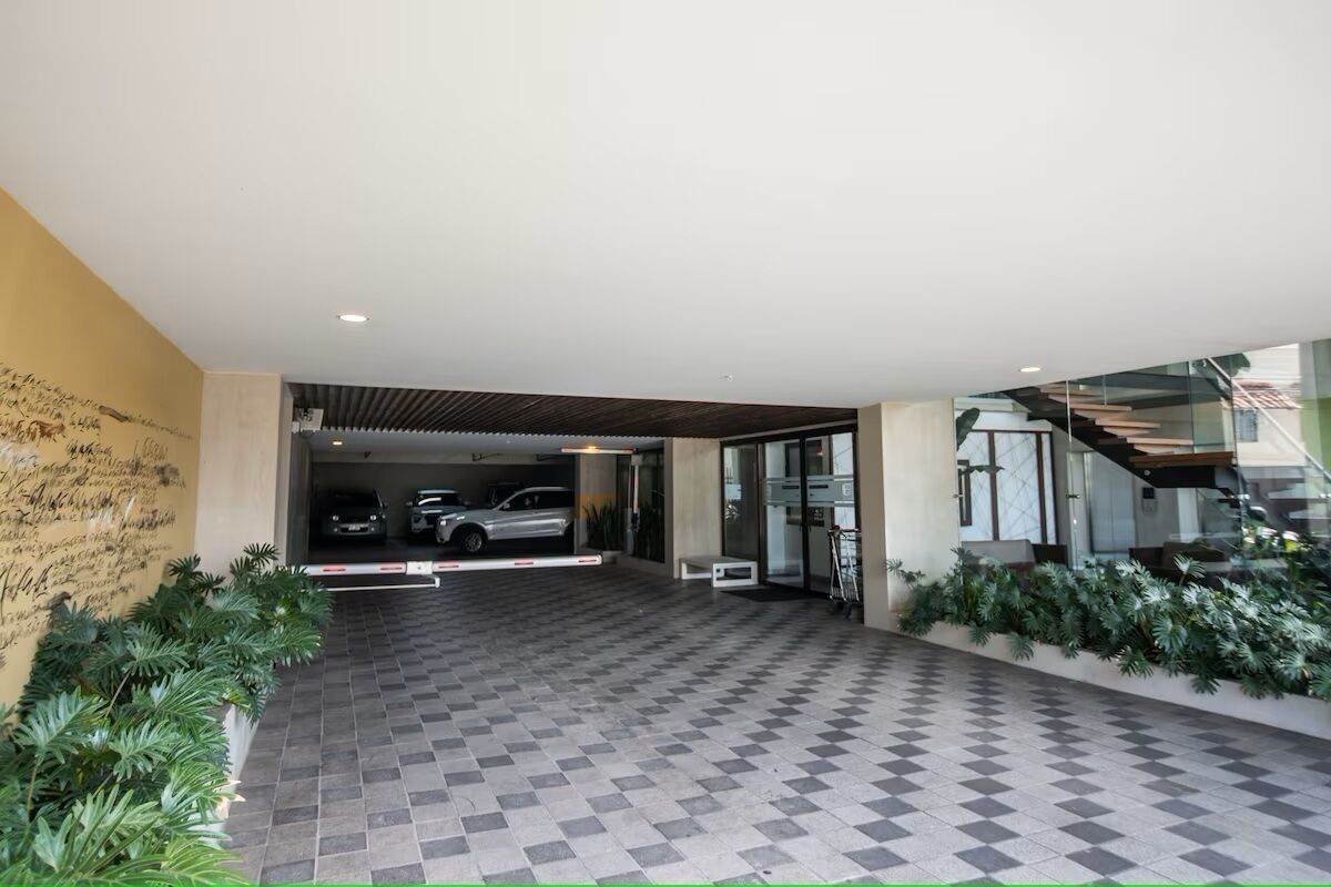 A modern hotel entrance with a checkered floor, a covered parking area, and a staircase leading to the upper floors.