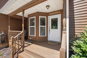 A wooden house with a covered porch, a white door with a glass window, and a welcome sign above the door.