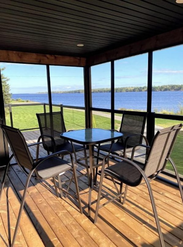 A covered outdoor seating area with a table and chairs, overlooking a body of water.