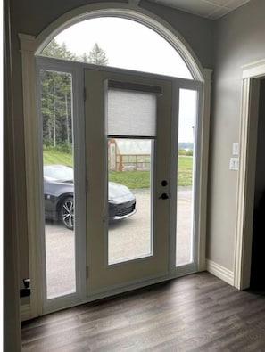 A door with a view of a car outside, a window with a blind, and a wooden floor.