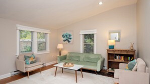 A living room with a green sofa, a white coffee table, and a bookshelf. - Cheerful two bedroom cottage with Parisian patio! (Middletown)