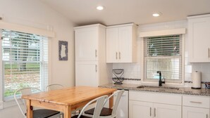 A modern kitchen with white cabinets, a wooden table, and white chairs. - Cheerful two bedroom cottage with Parisian patio! (Middletown)