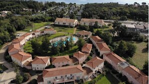 Un área residencial costera con casas escalonadas, una piscina central y vista al mar.
