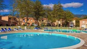 Una piscina con sillones de descanso y un cielo azul despejado.