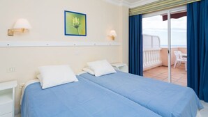 Camera d'albergo con due letti, un balcone con ringhiera bianca e vista sul mare.
