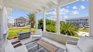 Overdekt terras met witte meubels, een bankje en uitzicht op een woonwijk met huizen en palmbomen.