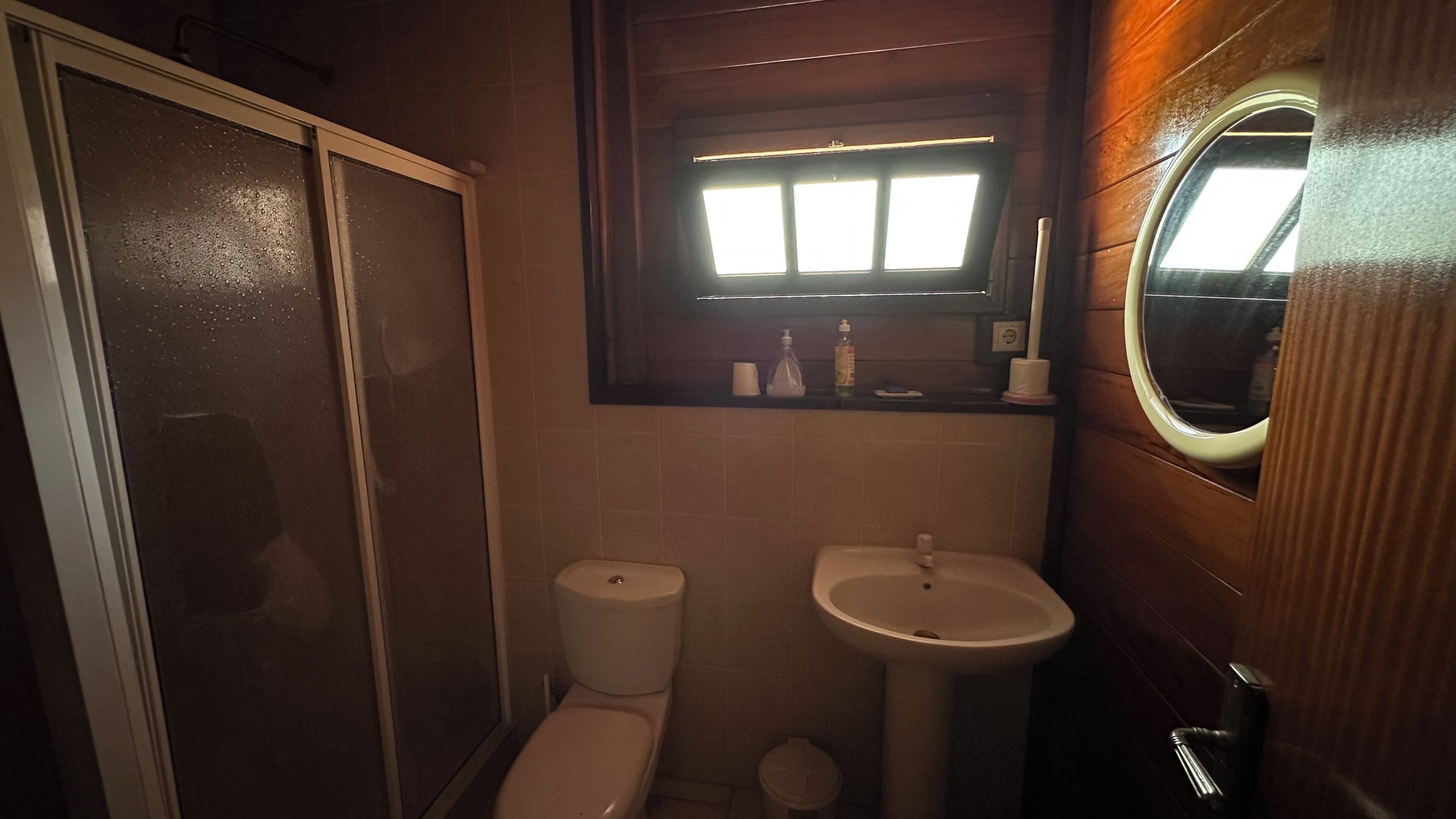 Een compacte badkamer met toilet, wastafel en een raam boven de wastafel.